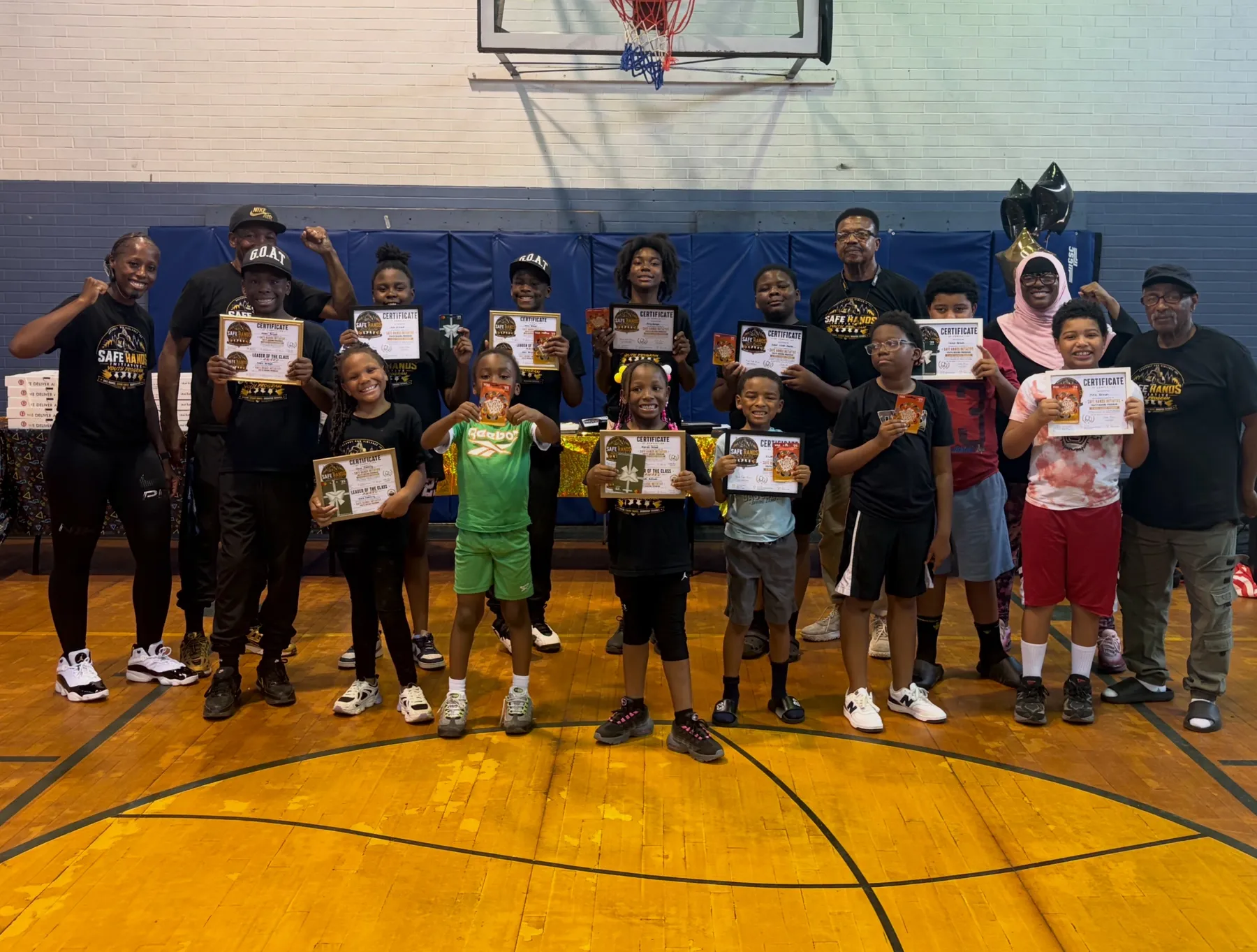 Youth boxing programme participants holding certificates and raising fists in a gymnasium.